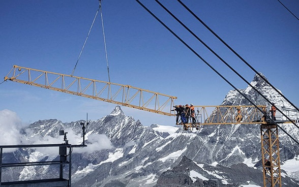 Sept personnes installent une grue pour construire un téléphérique.